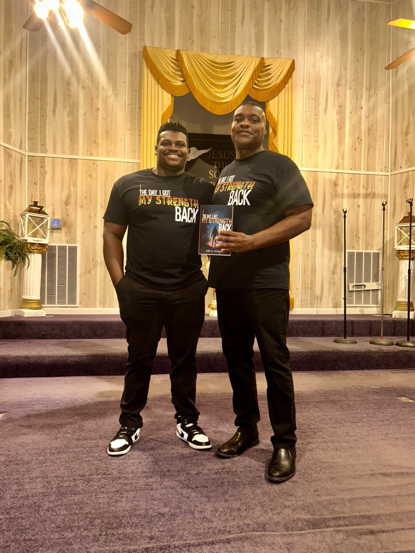Dr. Eric D. Edwards holding The Day I Got My Strength Back with a reader in matching book shirts at church